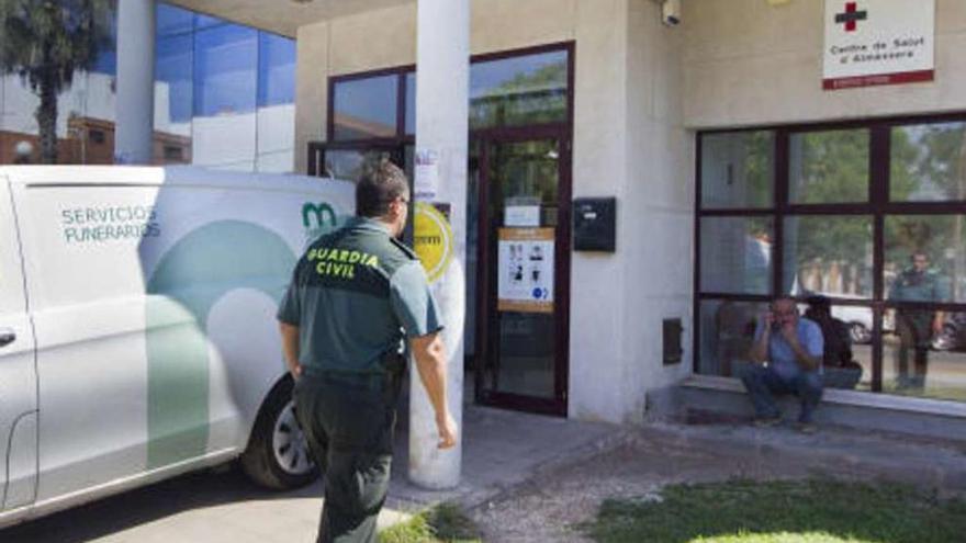 Un agente pasa ante el vehículo de la funeraria en el Centro de Salud de Almàssera.