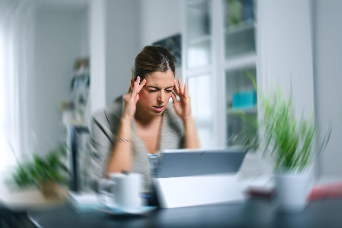 UNA MUJER SE PRESIONA LAS SIENES PARA ALIVIAR SU DOLOR DE CABEZA. Sick dizzy young woman suffering headache while working on her laptop at home. FOTO DE RECURSO. DOLENCIA. MIGRAÑAS. CEFALEAS. ESTRES