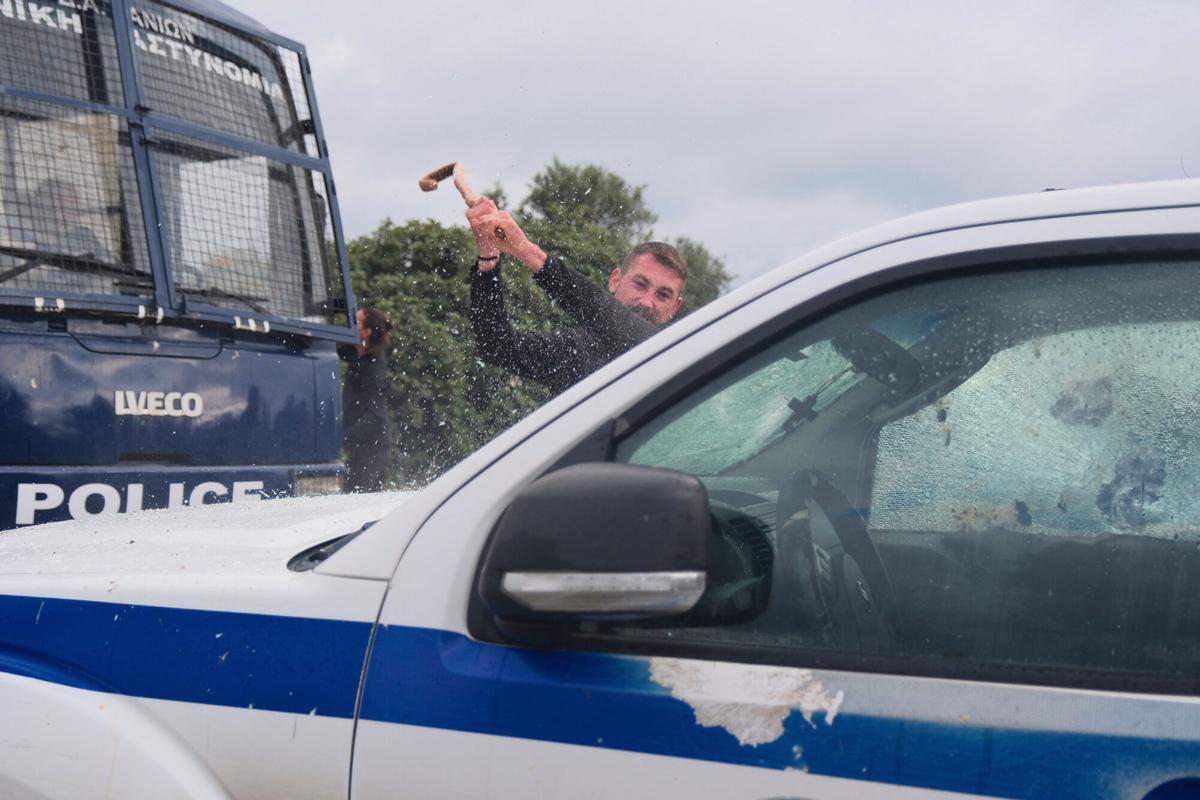 A protester breaks the window of a police vehicle during clashes with officers blocking their march to Chanias airport on Crete, Greece, Monday, Dec. 8, 2025, amid protests over delayed EU farm subsidies. (AP Photo/Giannis Angelakis)