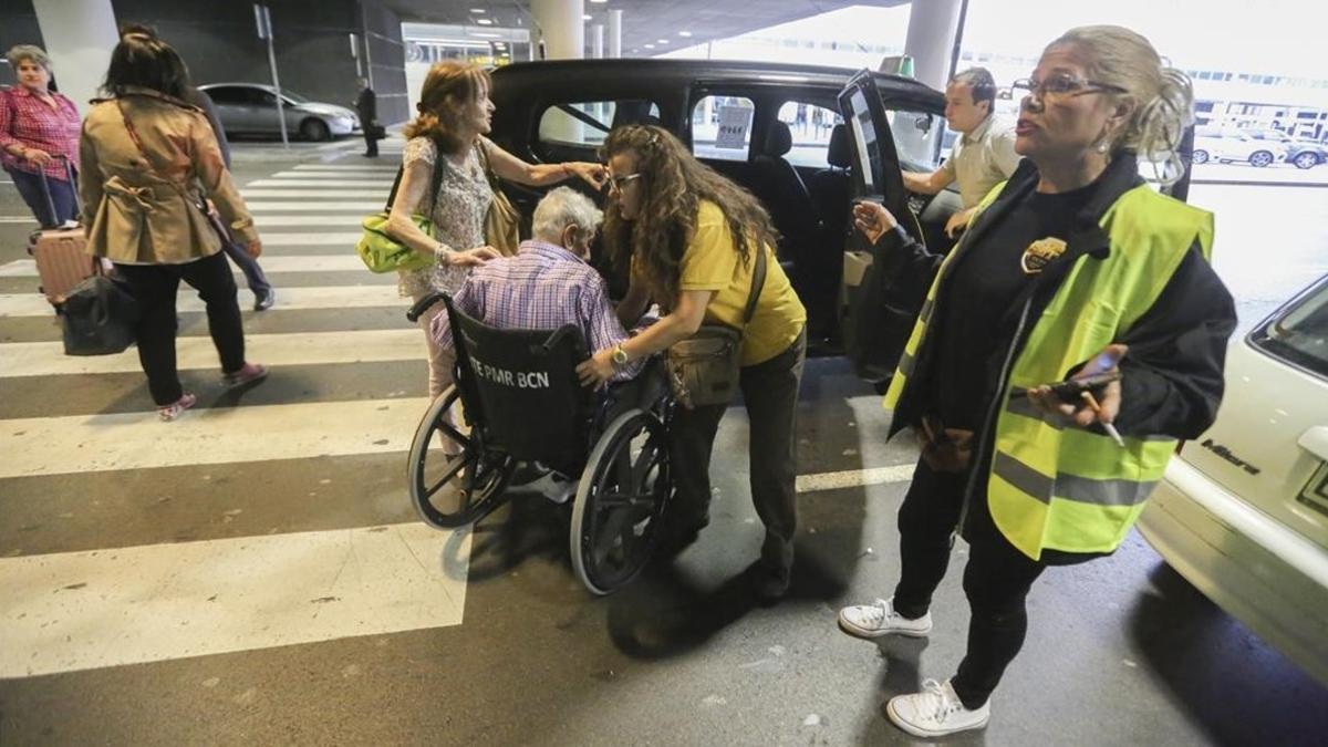 Un taxista en servicios mínimos en la jornada de huelga ayuda a subir al vehículo a un usuario en silla de ruedas en el aeropuerto de El Prat.