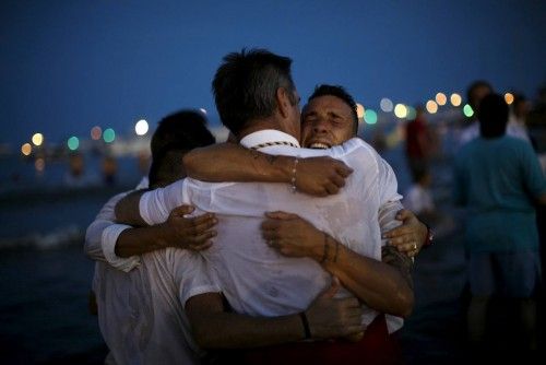 Men in traditional costumes embrace after carrying a statue of the El Carmen Virgin into the sea during a procession in Malaga