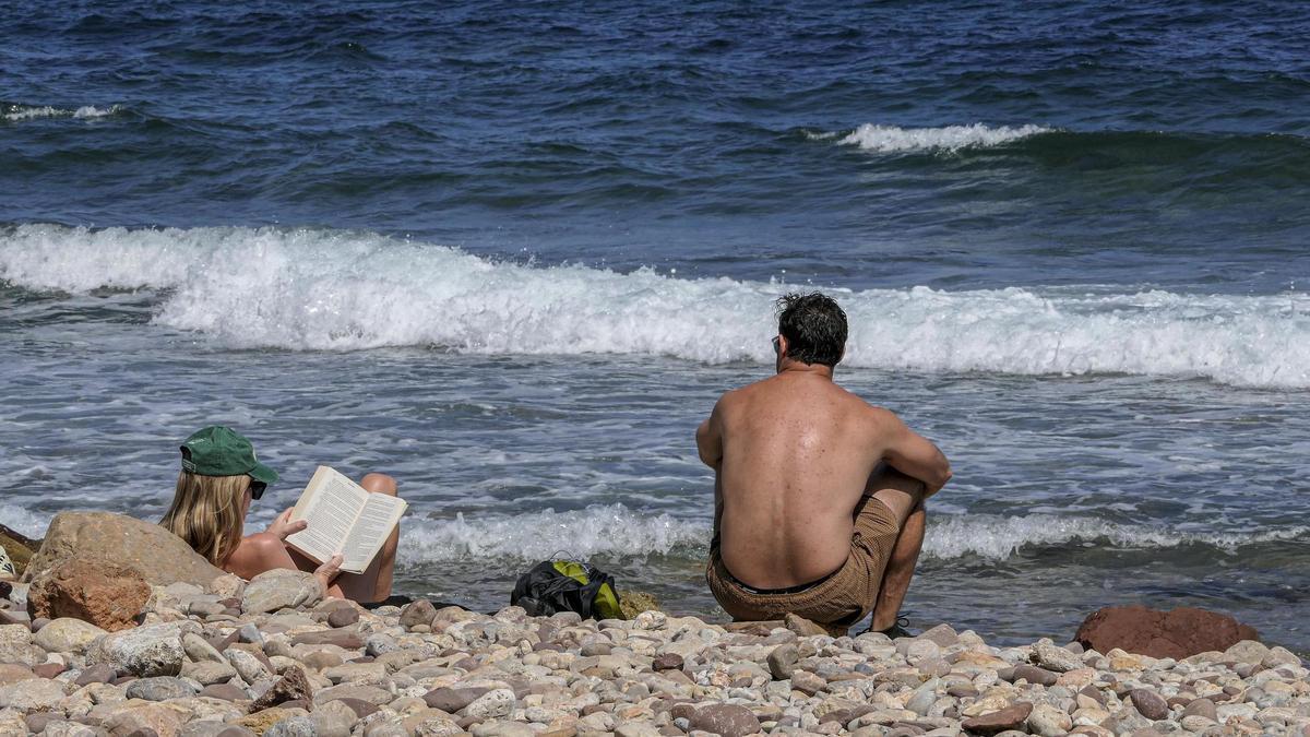 Ein Paar blickt an der Küste von Banyalbufar aufs Meer und liest.