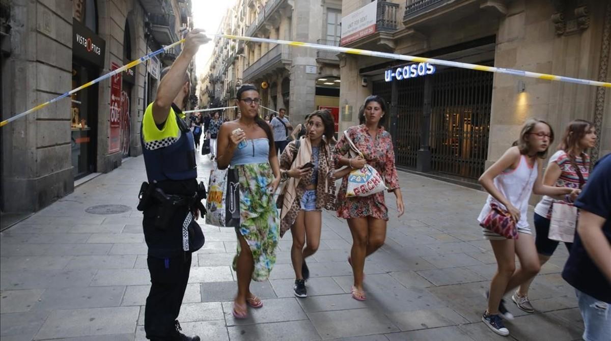 Unos turistas pasan bajo un cordón policial en la calle de Portaferrissa.