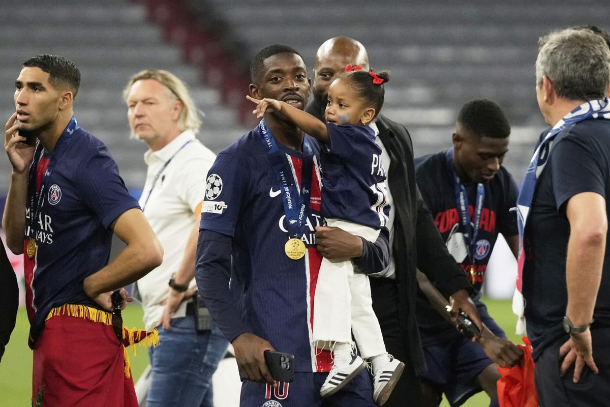 PSG's Ousmane Dembele carries a child on the pitch after winning the Champions League final soccer match between Paris Saint-Germain and Inter Milan at the Allianz Arena in Munich, Germany, Saturday, May 31, 2025. (AP Photo/Luca Bruno)