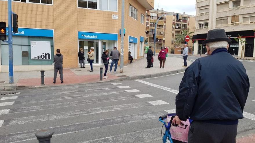 Gente esperando ante una sucursal bancaria hoy en Alicante.