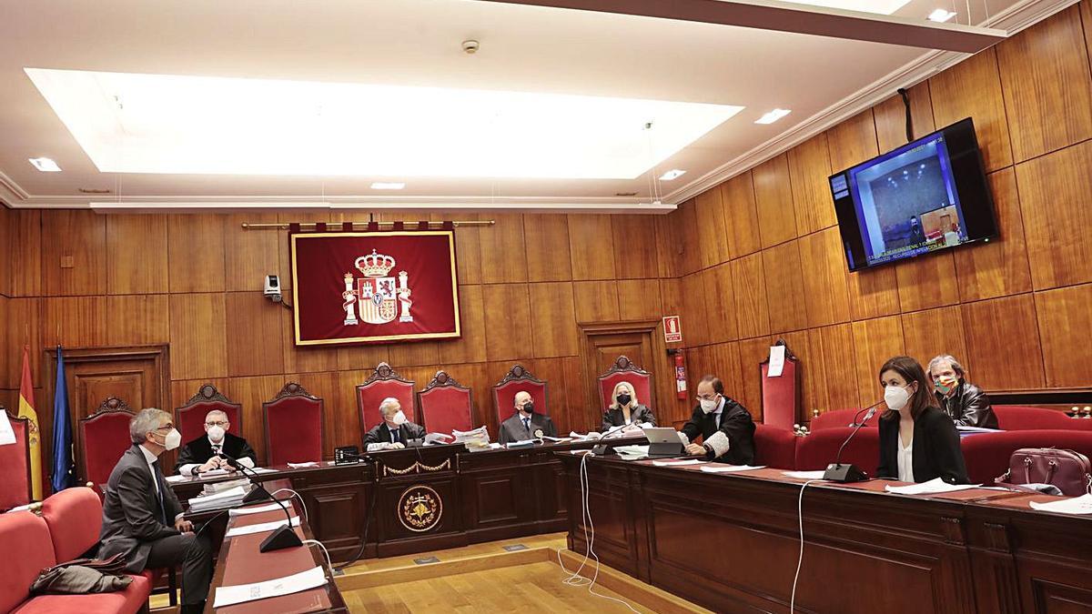 Vista general de la Sala, con el tribunal al fondo y el acusado en la pantalla de televisión en videoconferencia desde el centro penitenciario de Asturias. | Miki López