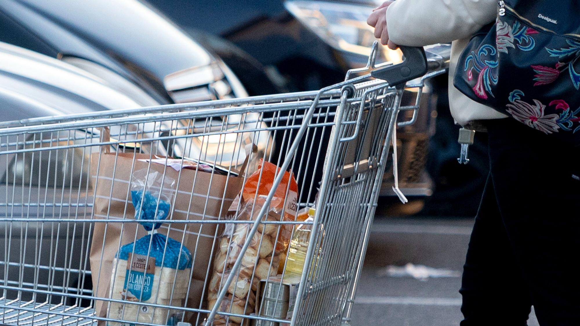 Una mujer va por un aparcamiento de un supermercado con un carro de la compra.