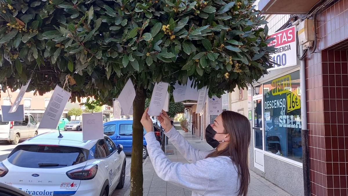 Noelia Vivero, leyendo una de las poesías que cuelgan de los árboles de la plaza Venancio Pando, en Arriondas. | M. V.