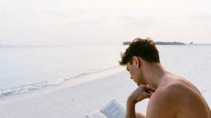 Un hombre lee mientras está sentado en la playa.