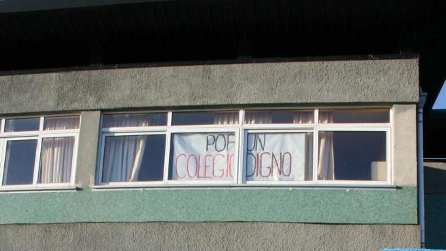 Una niña accede al colegio, en una de cuyas ventanas se ve un cartel de denuncia.