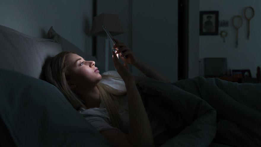 Una mujer mira su móvil antes de dormir.