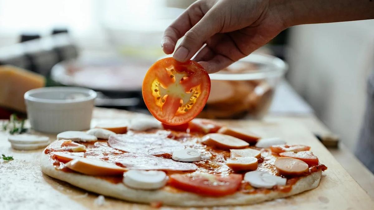 Persona añadiendo tomate en una pizza.
