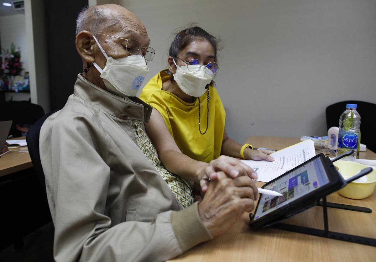 Yongyuth Napasab, de 94 años, aprende a usar un dispositivo electrónico junto a una de sus cuidadoras en la residencia donde vive