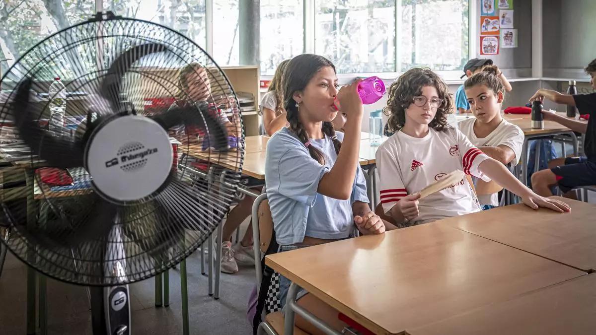 Una menor bebe agua en un aula con ventiladores portátiles.
