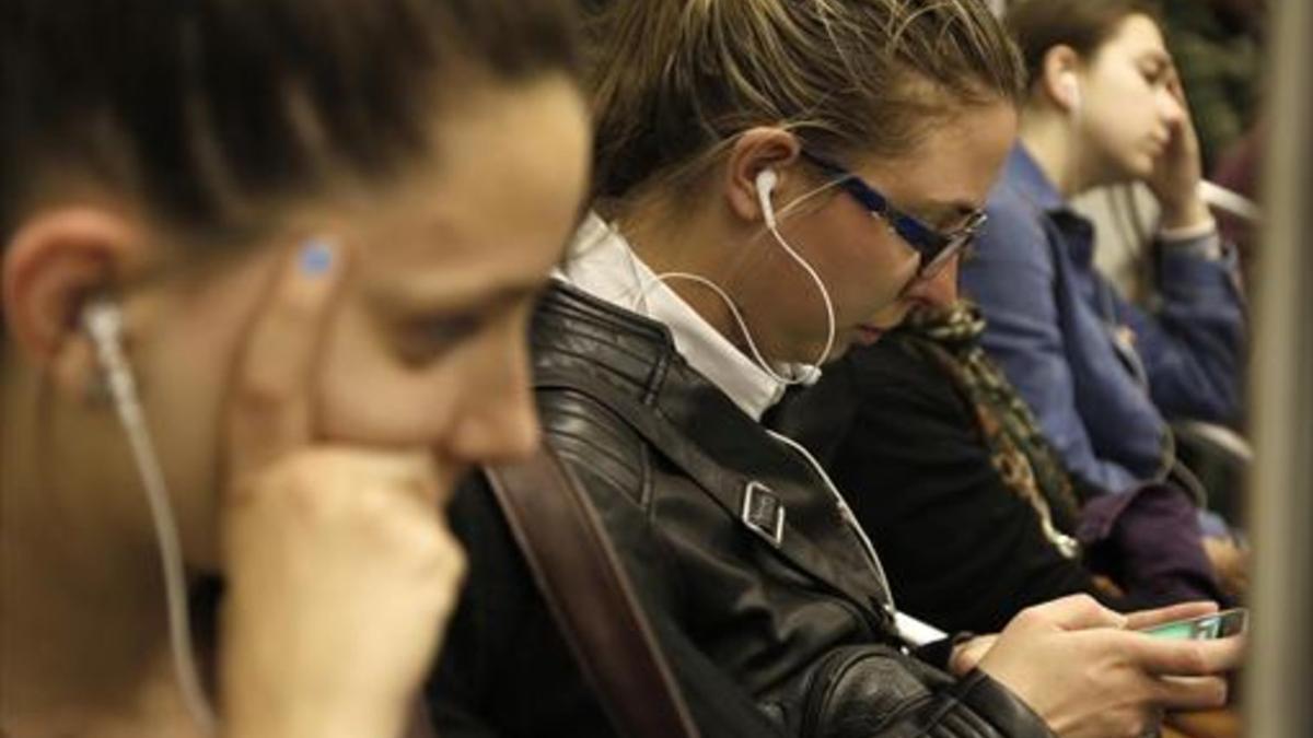 Jóvenes escuchando música con auriculares en el metro.