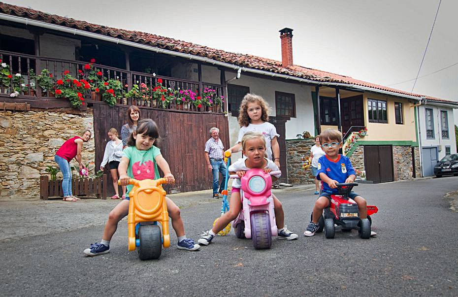 Jimena y Olivia Álvarez y sus primos Mateo y Amaia García juegan frente a la casa de su abuela mientras sus madres, Silvia García y Nuria Carbajal, y su abuelo Ángel Carbajal los vigilan junto a su prima Sara Rilo. | P. Martínez