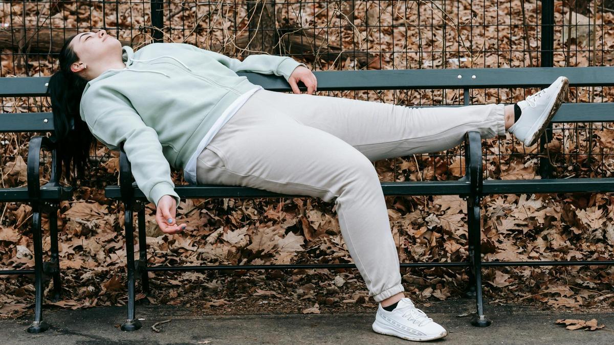 Una chica descansa en un banco en un parque lleno de hojas caídas por el otoño.