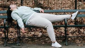 Una chica descansa en un banco en un parque lleno de hojas caídas por el otoño.
