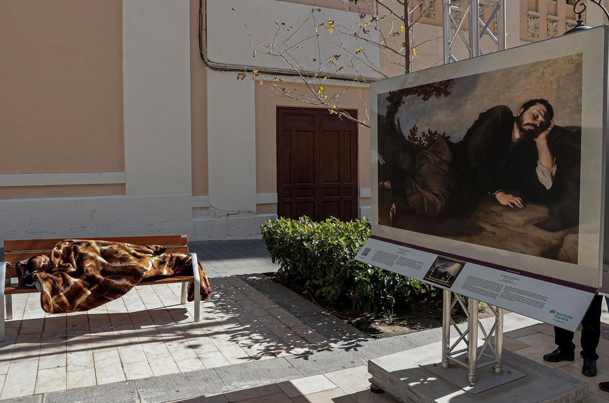 Una persona duerme sobre un banco junto a la imagen de una obra del Museo del Prado, instalada en la calle