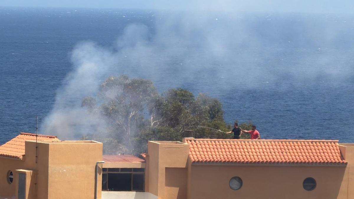Dos vecinos echan agua sobre las llamas en una vivienda de Las Caletillas