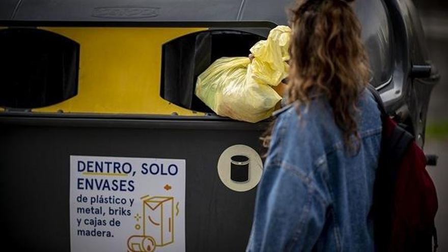 Una mujer deposita una bolsa en un contenedor de reciclaje.