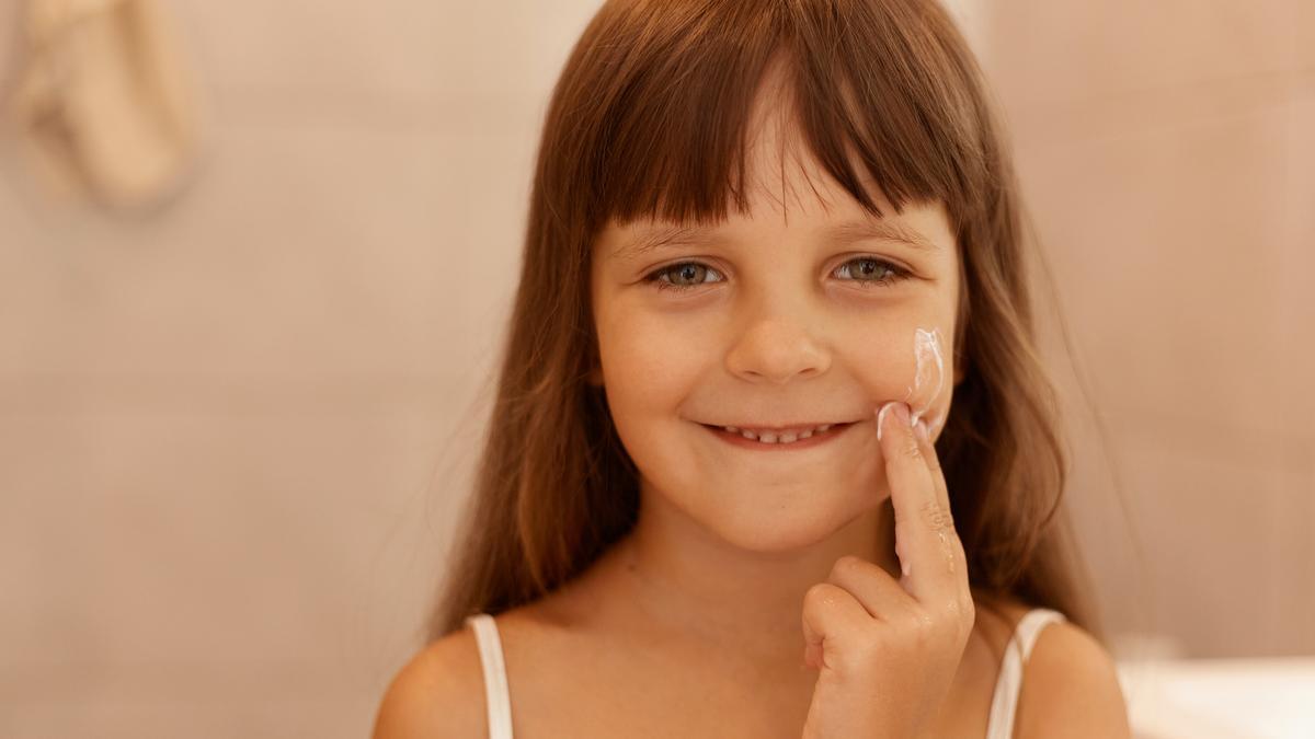 Una niña aplicándose crema hidratante.