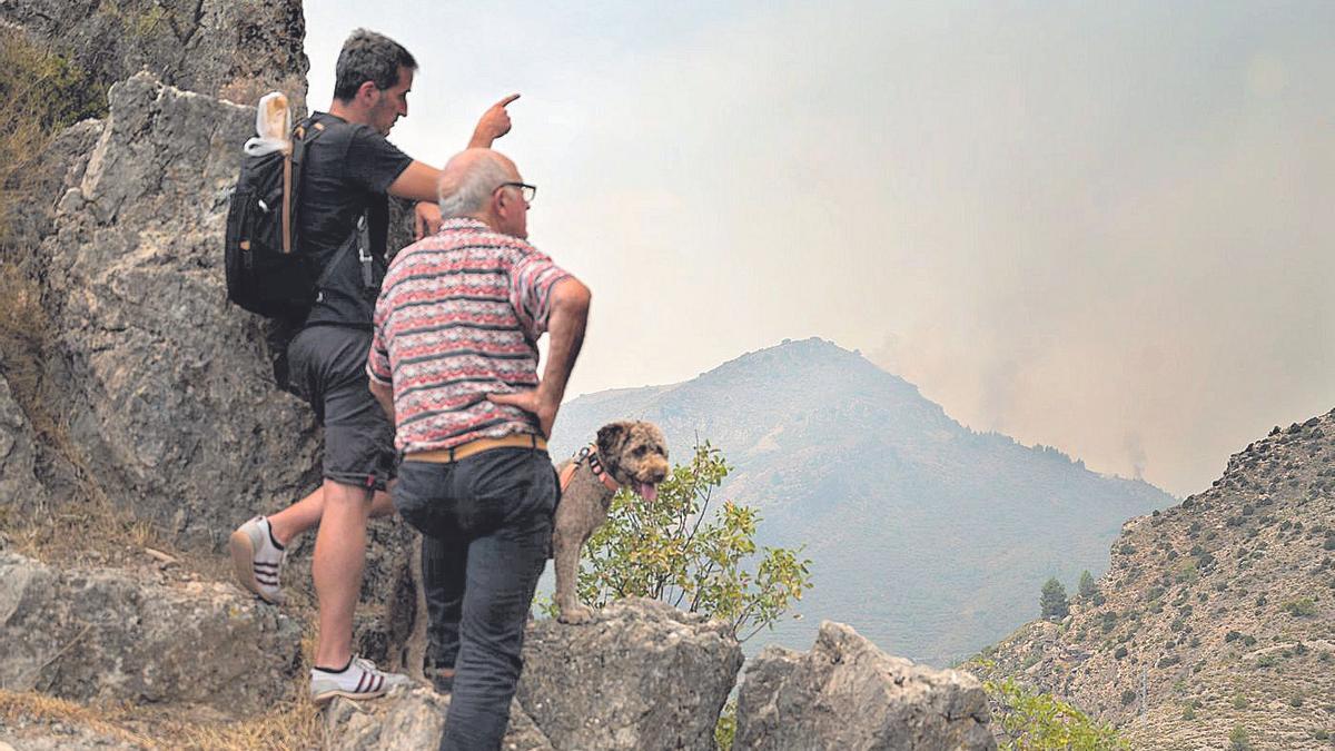 Dos personas observan la evolución del incendio forestal de Bejís, días atrás, cuya evolución cubre Medi TV.