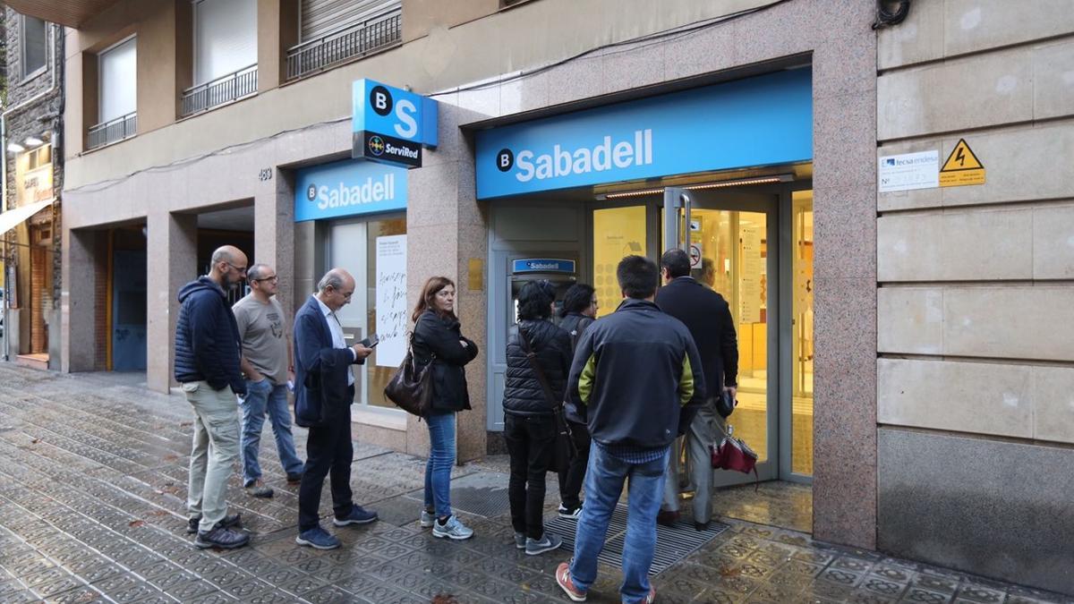 Una decena de persona hacen cola en un cajero del Banc Sabadell, este viernes a primera hora de la mañana.