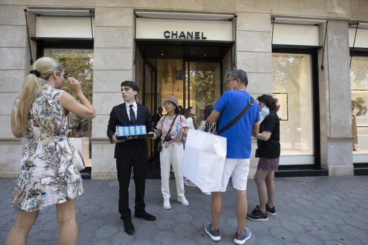 Clientes haciendo cola para entrar en la tienda de Chanel de paseo de Gràcia (Barcelona) mientras un empleado les ofrece agua para aguantar el calor.