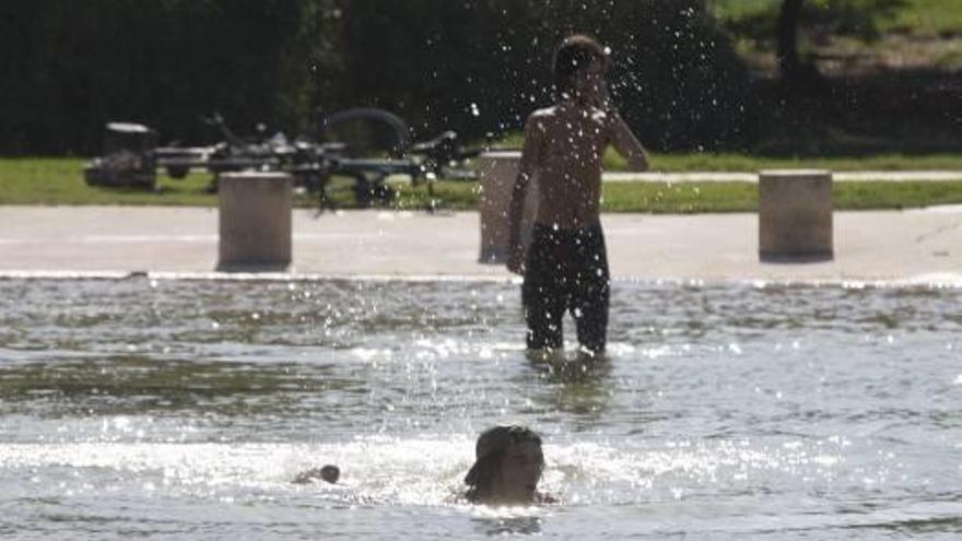 Dos jóvenes se refrescan en un estanque del Jardín del Turia.