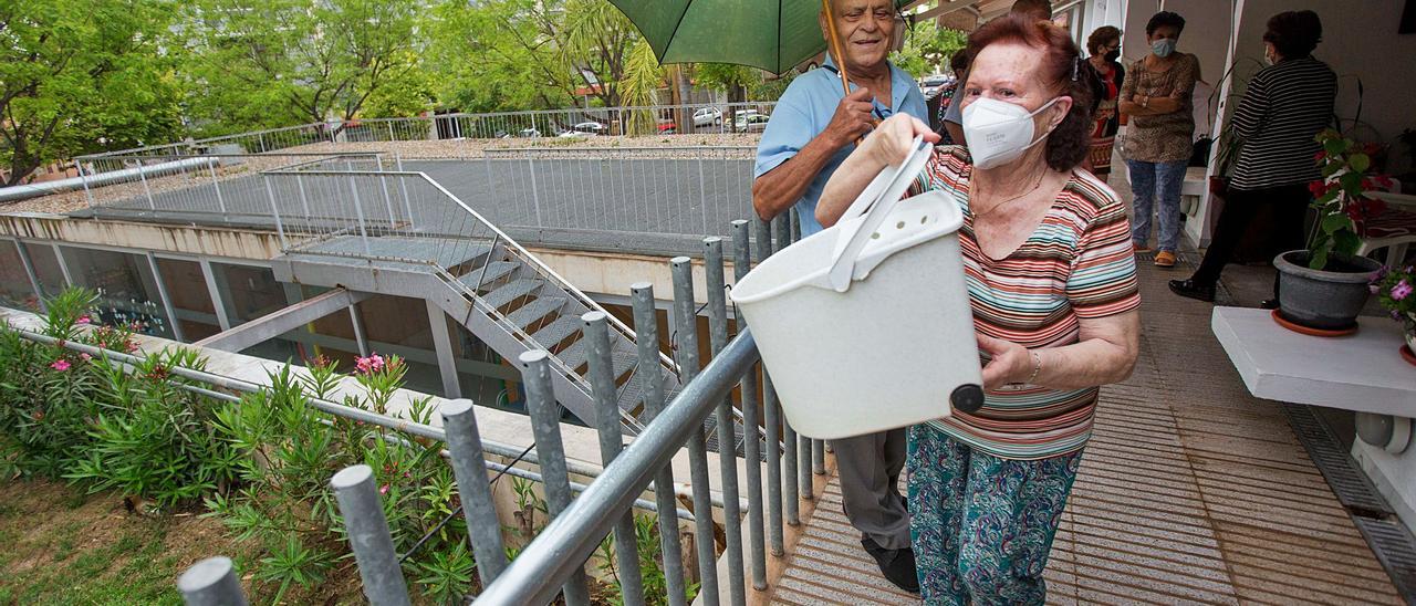 Una mujer echa agua con lejía en el jardín para paliar los malos olores de los orines que sufren en la pared anexa a sus viviendas, ante la mirada de sus vecinos. | JOSE NAVARRO