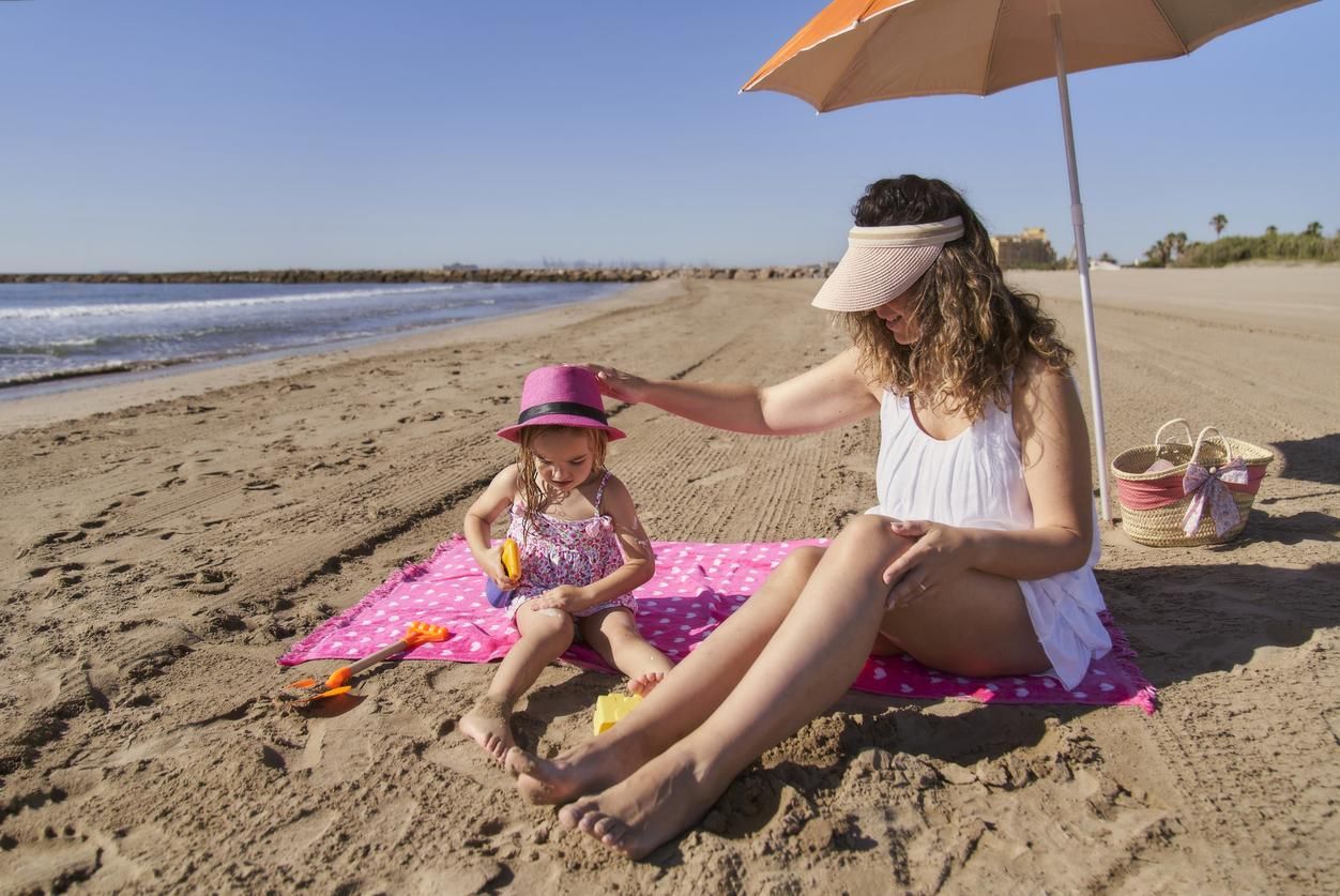 Una niña poniéndole crema solar a su madre en la playa.