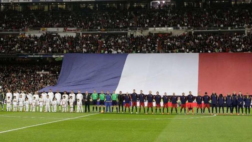Jugadores, entrenadores y árbitros posan ante una bandera de Francia durante el minuto de silencio.