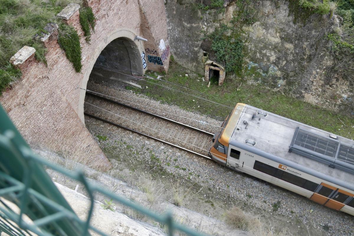 Vista des d'un talús d'un tren de l'R1 entrant en un túnel en un tram on hi ha circulació per via única.