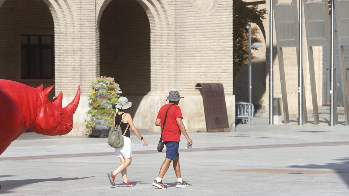 Una pareja camina bajo el sol en la plaza del Pilar