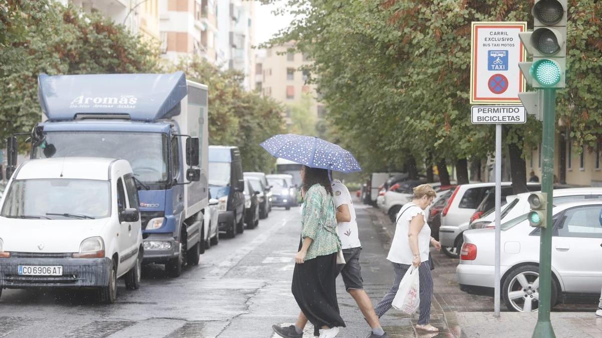 Peatones se protegen de la lluvia con un paraguas en una calle de Ciudad Jardín en Córdoba.