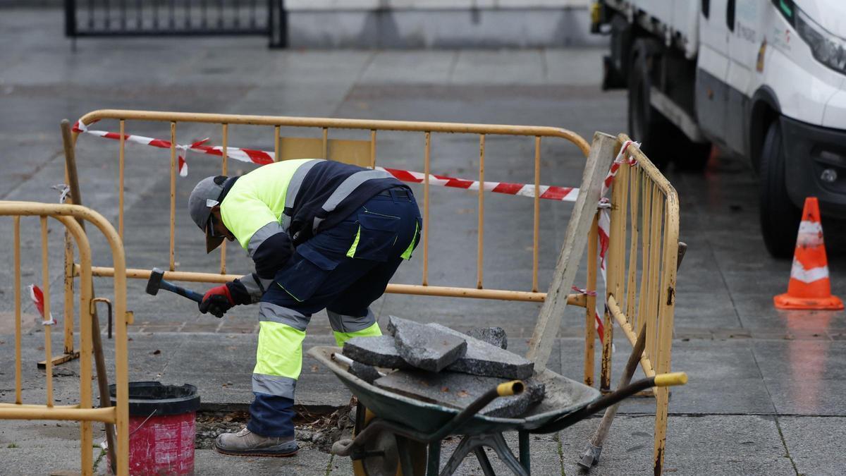 Un trabajador encorvado mientras trabaja rompiendo losetas de una calle.