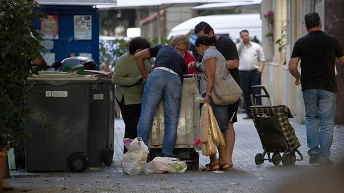 Varias personas recogen comida caducada de los contenedores de un supermercado, en Barcelona.