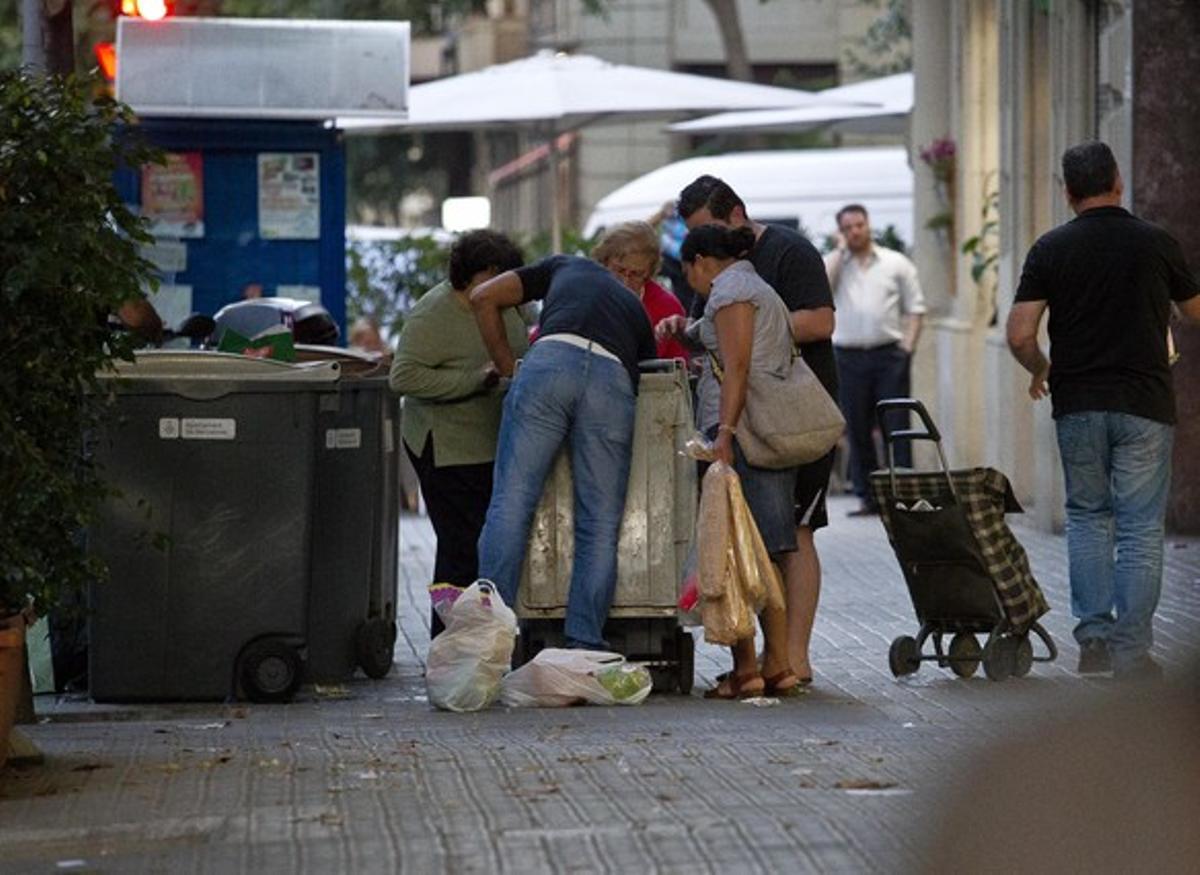 Varias personas recogen comida caducada de los contenedores de un supermercado, en Barcelona.