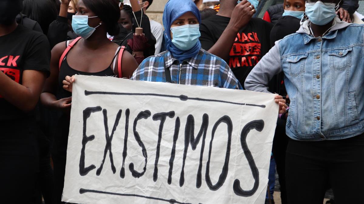 Una manifestant sosté una pancarta que diu &#039;Existimos&#039; en la concentració contra el racisme a la plaça Sant Jaume de Barcelona