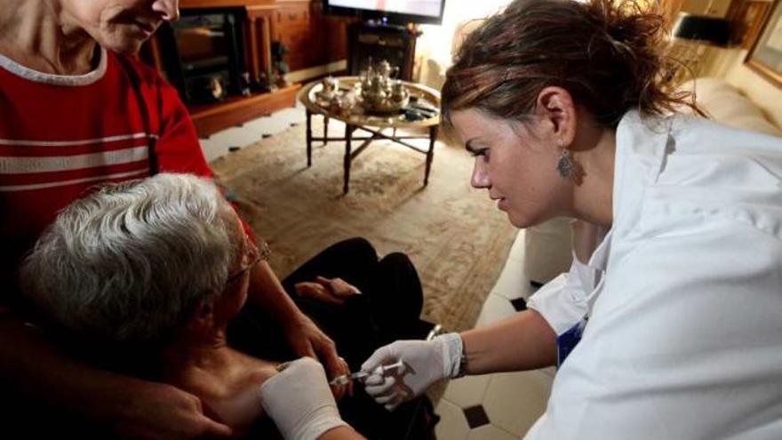 Una enfermera de Atención Primaria vacuna a una mujer de avanzada edad en su domicilio.