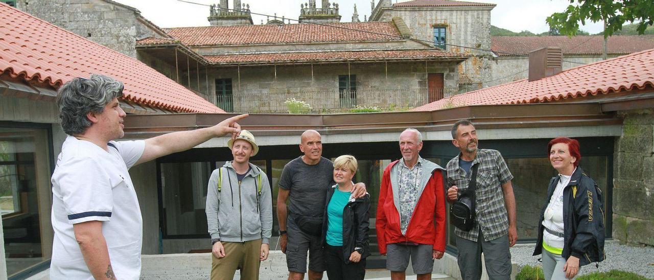 Uno de los hospederos, Iago De Juana, con un grupo de peregrinos, ante el nuevo albergue de Oseira, con el monasterio detrás.