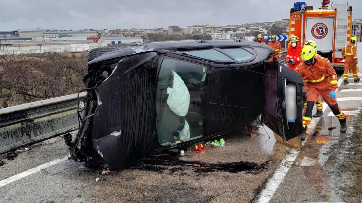 Bomberos revisan el coche, totalmente volcado, después del accidente registrado en la Pobla del Duc.