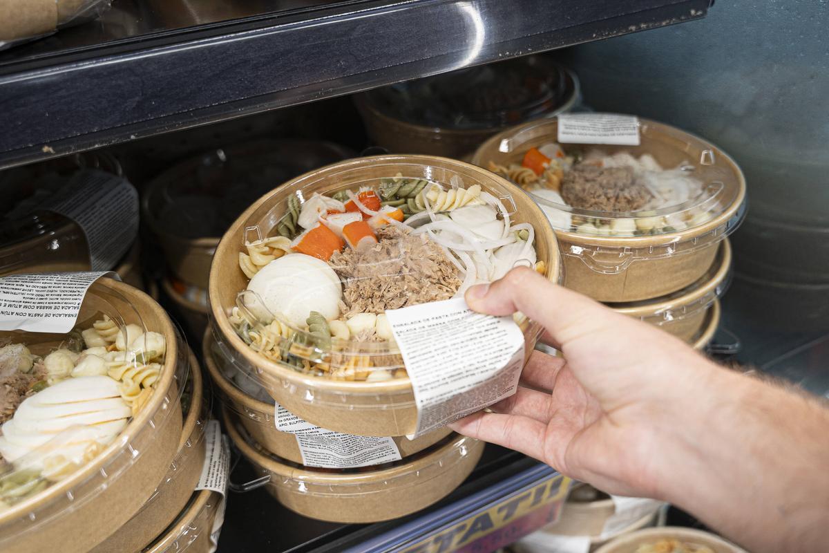 Una persona coge una ensalada de pasta, atún y huevo ya preparada en un supermercado.