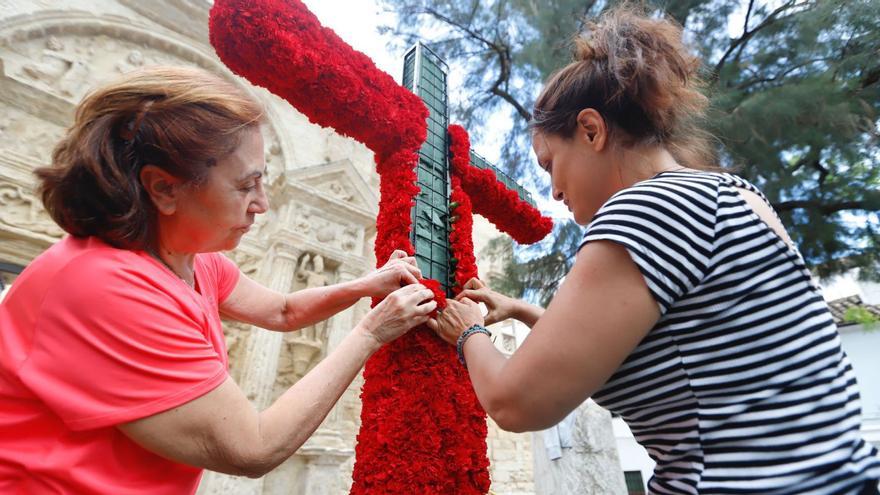 Dos voluntarias en una cruz, en la plaza de Jerónimo Páez, forran de claveles rojos una estructura para participar en el Concurso Municipal de Cruces. | MANUEL MURILLO