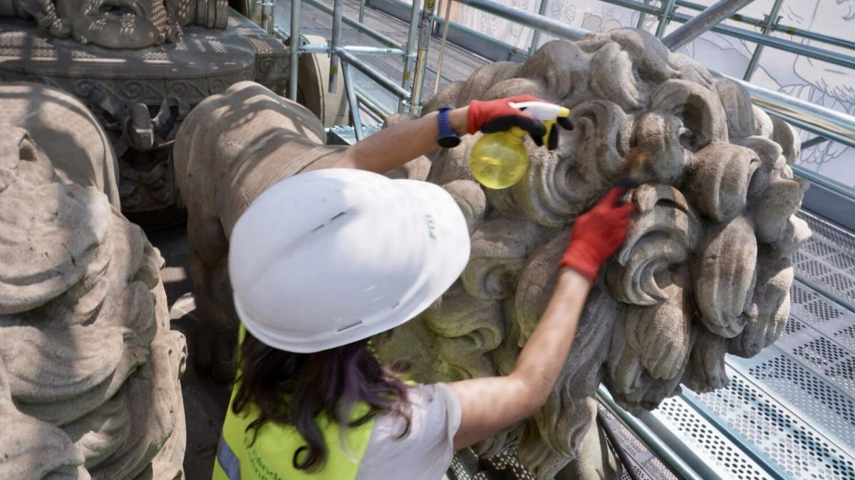 Restauradora limpiando con pulverizador y paño la melena de uno de los leones de la Fuente de Cibeles