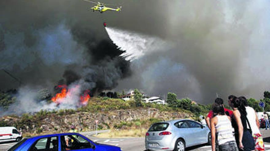 Un helicóptero intenta sofocar el fuego que amenaza unas casas en la entrada del municipio de As Neves