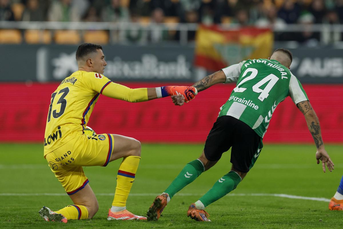 SEVILLA, 21/12/2025.- El delantero del Betis, Aitor Rubial (d), ayuda a levantarse al guardameta del Getafe, David Soria, durante el partido de la jornada 17 de LaLiga EA Sports, que Real Betis y Getafe CF disputan hoy domingo en el estadio La Cartuja de Sevilla. EFE/ Julio Muñoz