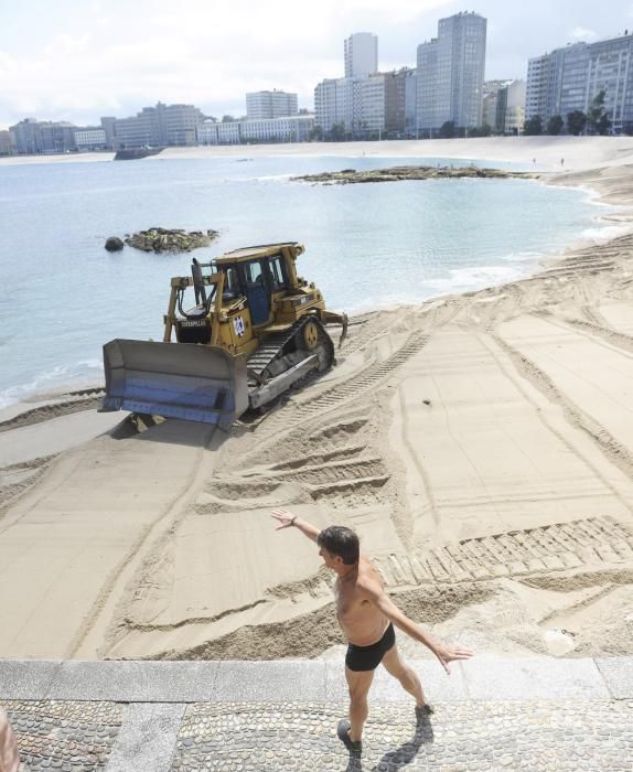 Las máquinas extienden la arena en la playa de Riazor.