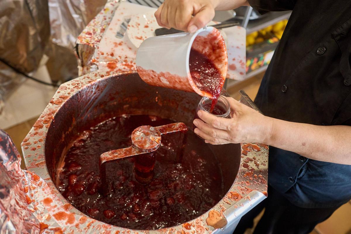 Treballadora omplint un pot amb melmelada de maduixa acabada de fer.